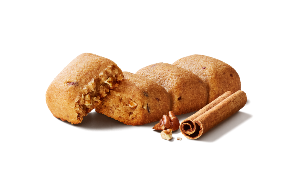 A GOOD TO GO Cinnamon Pecan Soft Baked Bar out of its wrapper, next to a cinnamon stick and a single pecan.