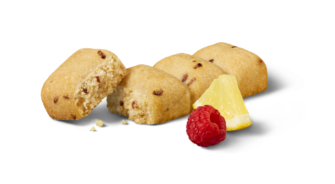 An individual GOOD TO GO Raspberry Lemon Soft Baked Bar, next to a single raspberry and a slice of lemon.